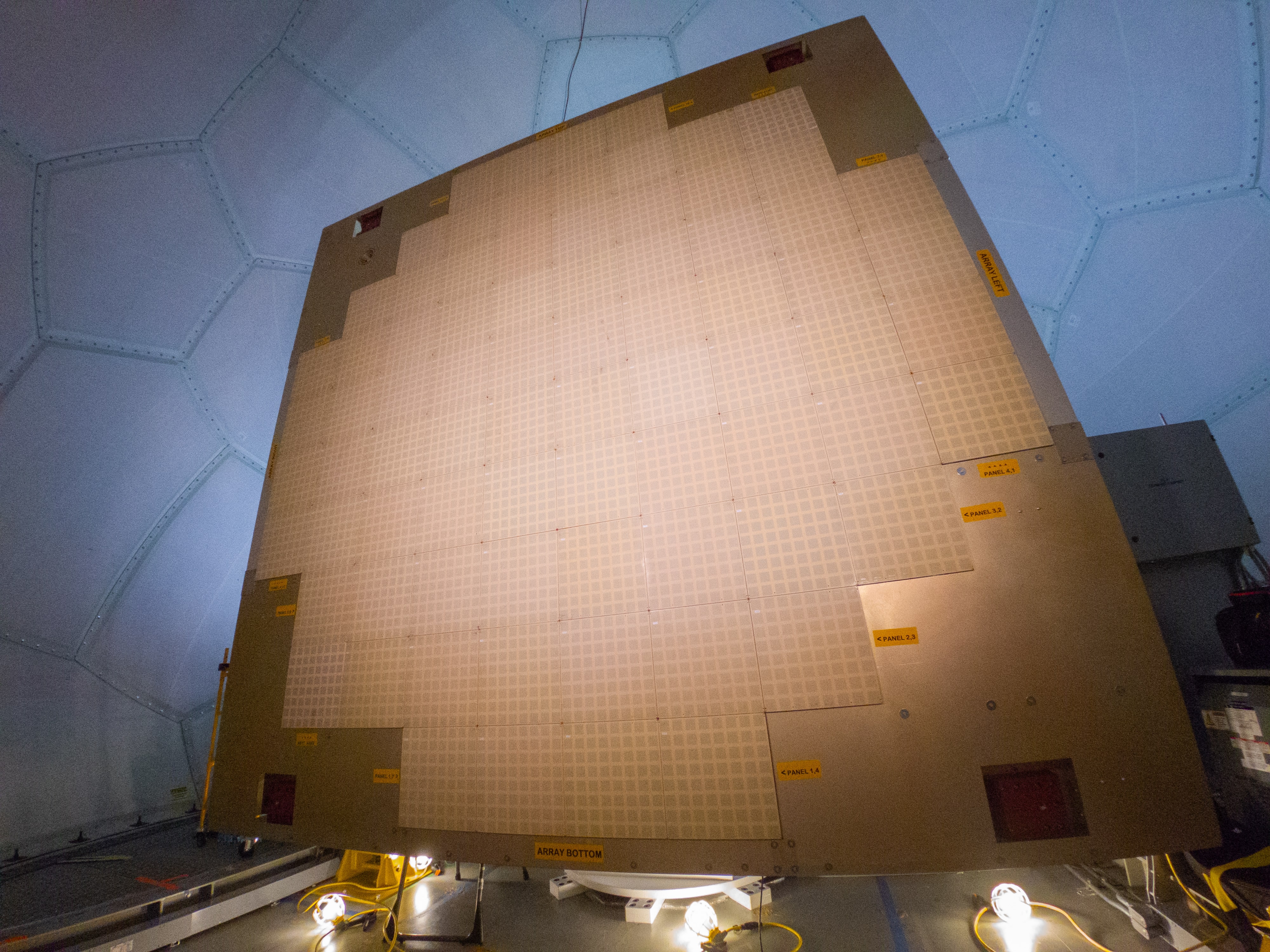 A flat, tan panel sits inside a radar dome. The large radar panel has 76 smaller panels comprising it on its flat surface.